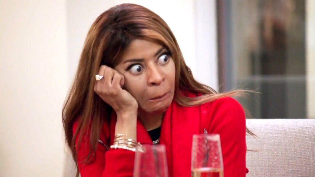 Mary Cosby in a red blazer reacting wide-eyed at the dinner table