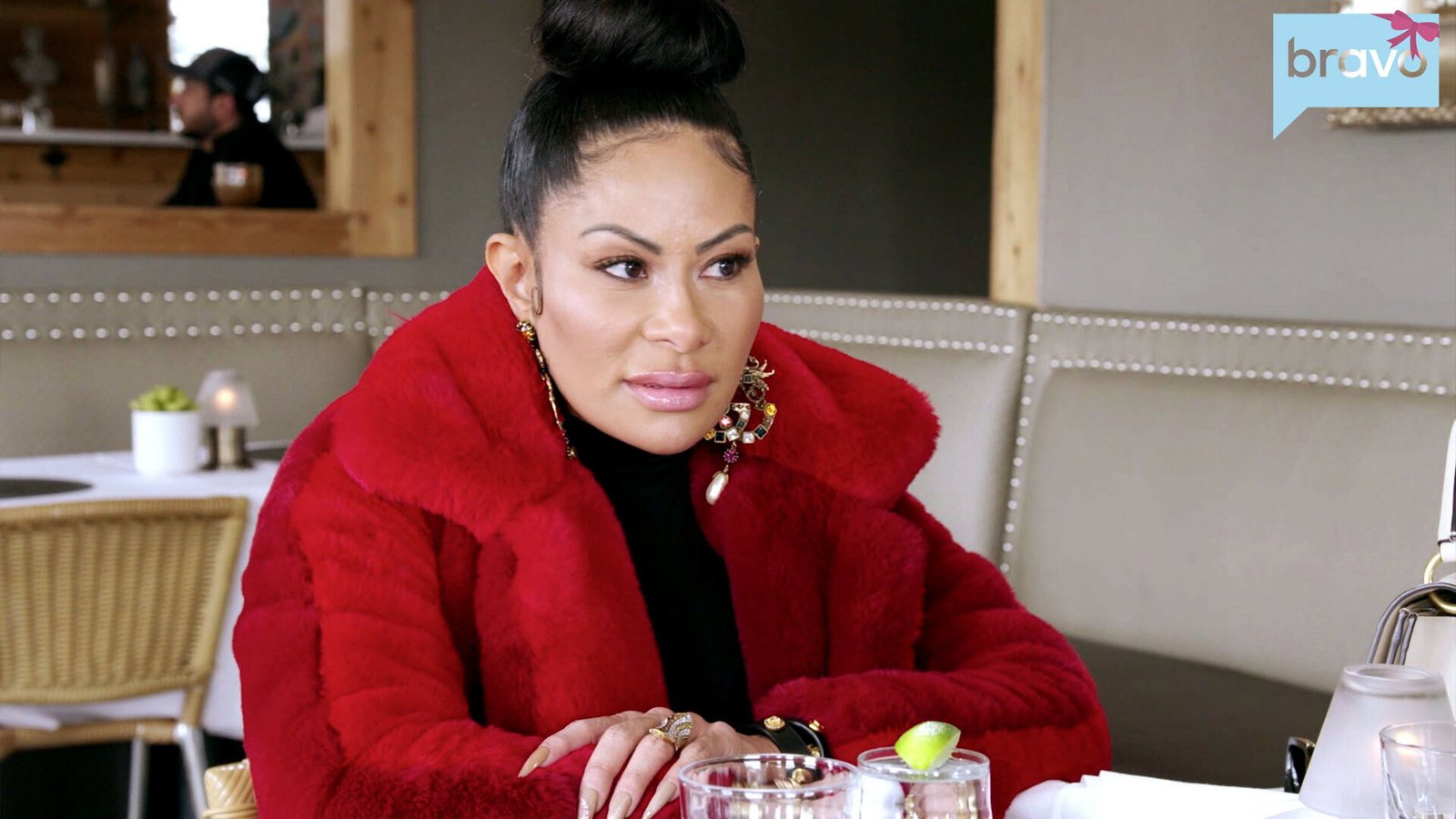 Jen Shah in a red fur coat listening at a restaurant table