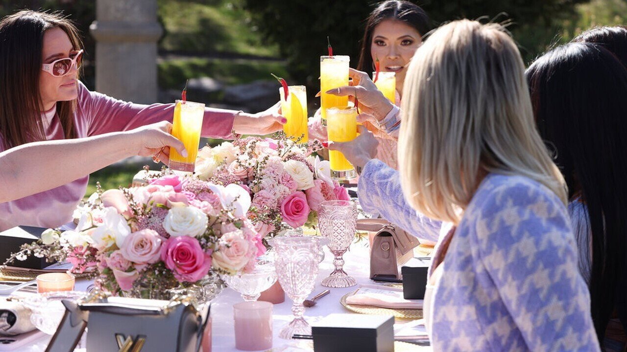 The women toast with yellow cocktails over a flower-covered table at the peace luncheon