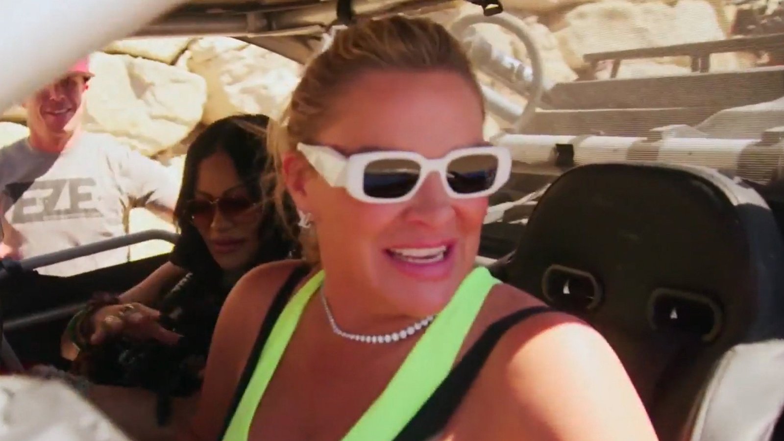 Heather Gay laughing in white sunglasses in an off-road vehicle, Jen Shah seated behind her