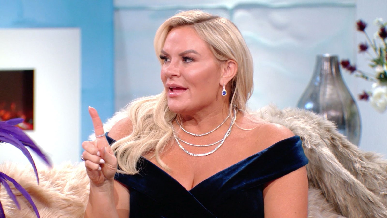 Heather Gay in a navy velvet dress on the reunion set, making a point with a raised finger