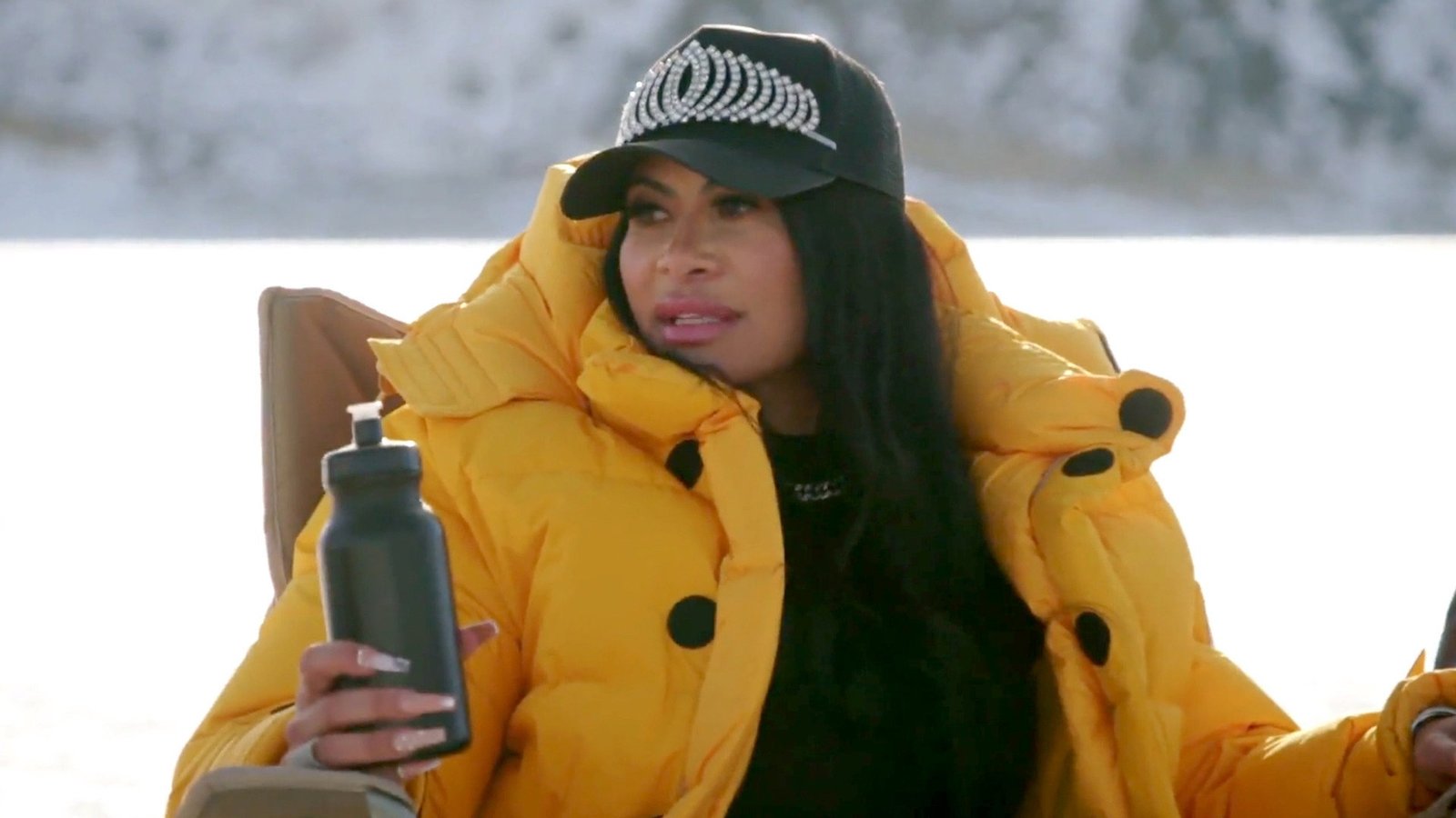 Jen Shah in a yellow puffer jacket and crown cap, holding a water bottle during the ice fishing trip in The Real Housewives of Salt Lake City