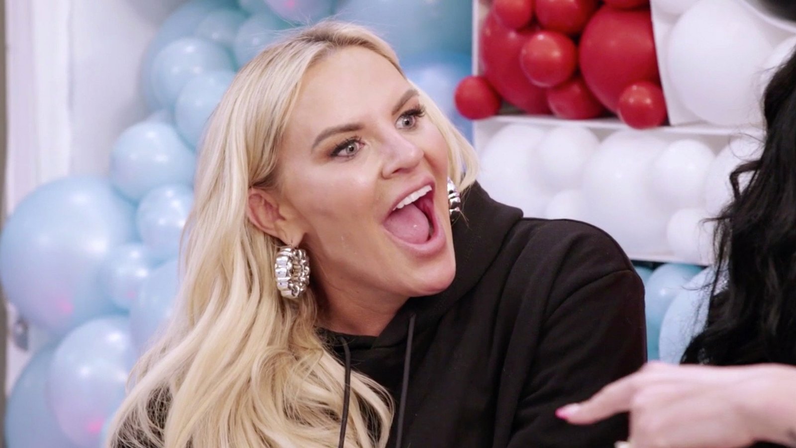 Heather Gay laughing in a black hoodie in front of red, white and blue balloons in The Real Housewives of Salt Lake City