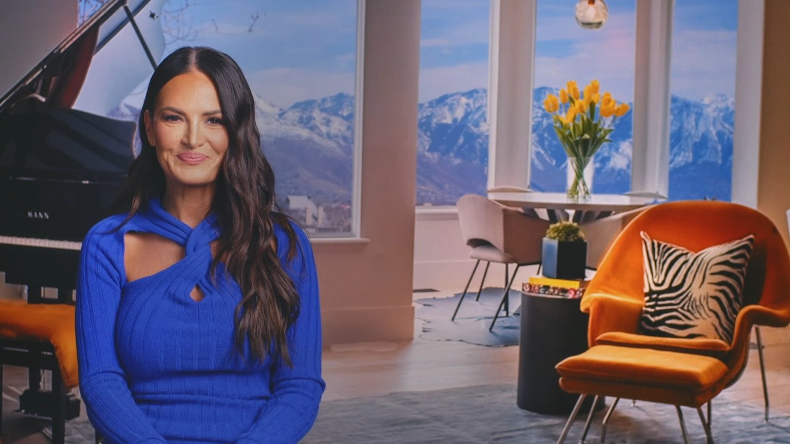 Lisa Barlow in a cobalt-blue dress in a confessional-style shot, mountains behind her