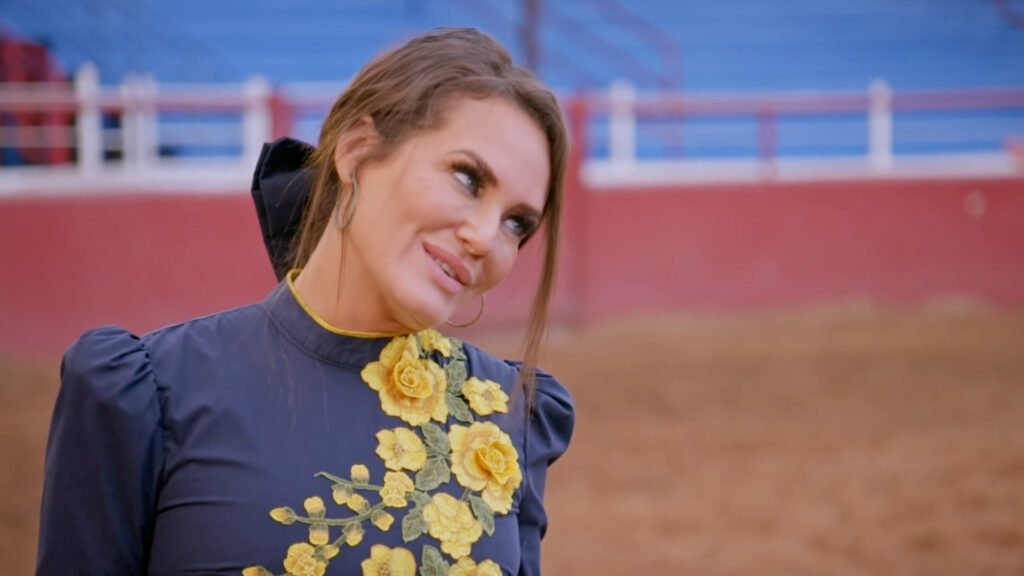 Meredith Marks in a navy floral-embroidered dress at the rodeo, glancing sideways