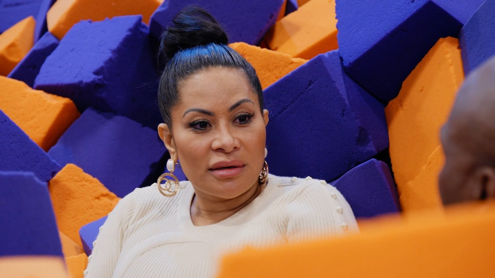 Jen Shah in a cream sweater seated in a foam pit, mid-conversation