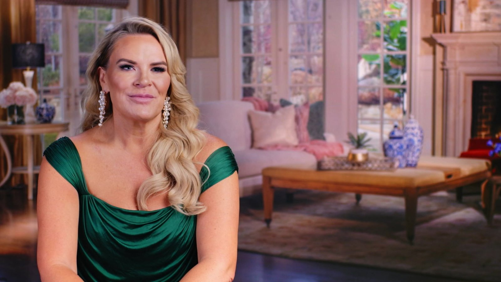 Heather Gay in an emerald dress and pearl-drop earrings, smiling in a confessional-style shot