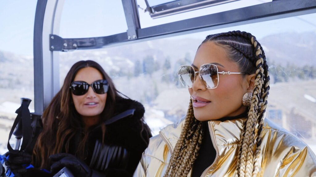 Jen Shah in a gold puffer jacket and braids beside Lisa Barlow in a ski gondola