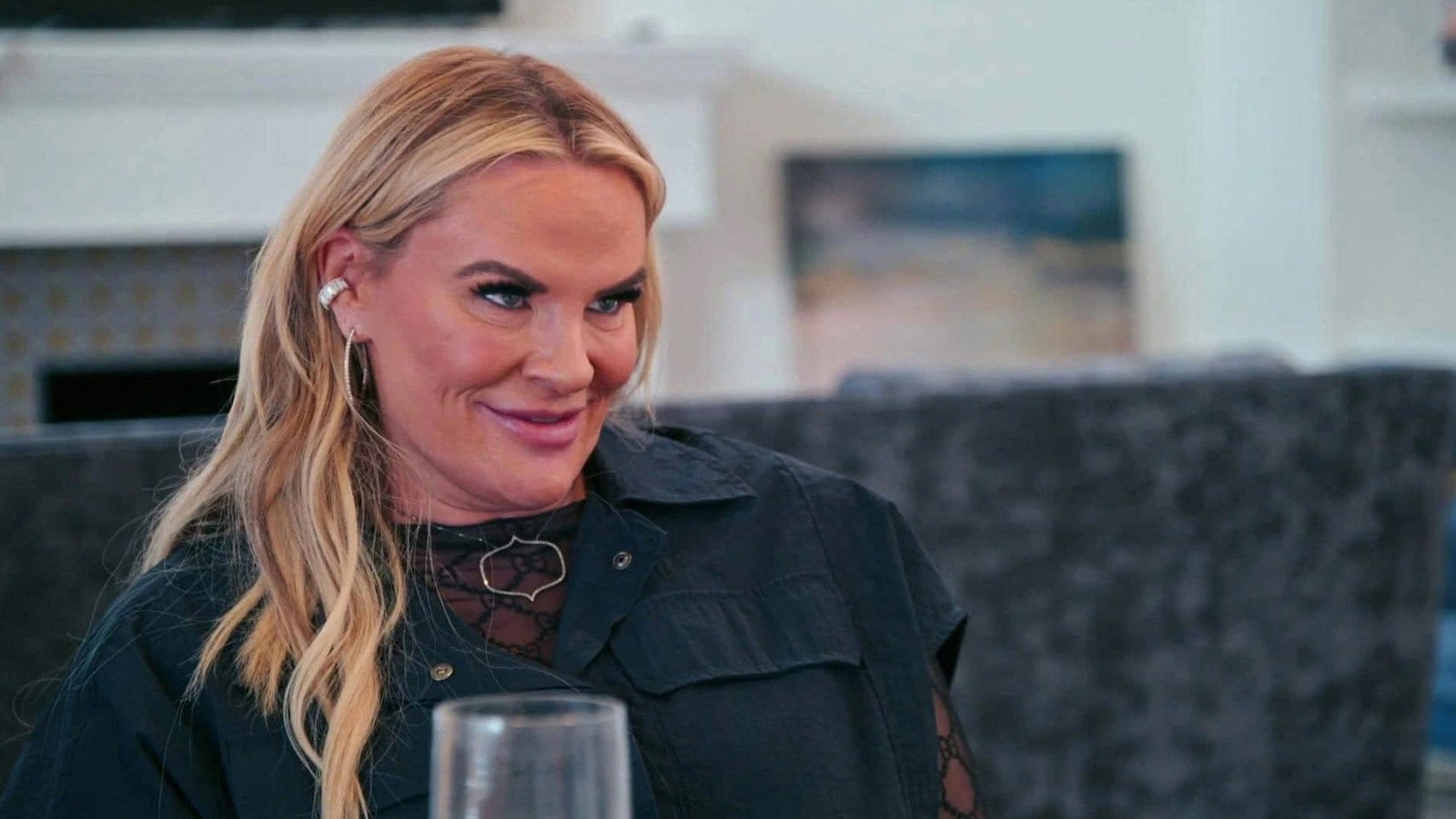 Heather Gay in a black top and hoop earrings, smiling over a glass at a gathering