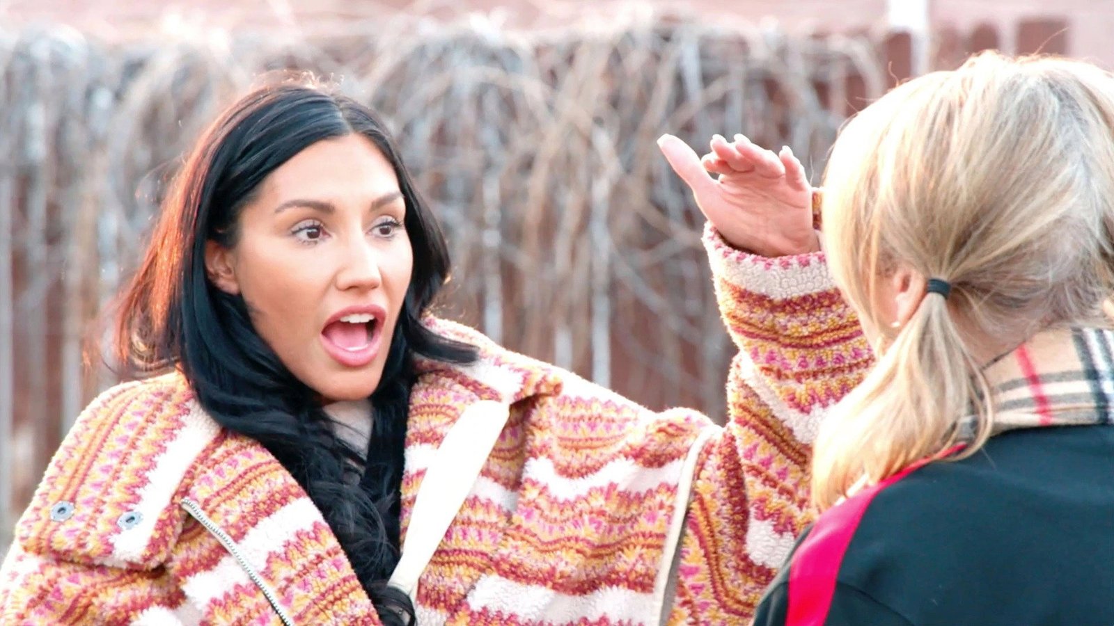 Monica Garcia in a patterned fleece coat, gesturing emphatically outdoors