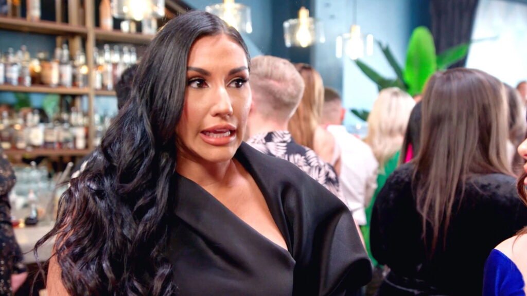 Monica Garcia in black at a crowded party, mid-conversation