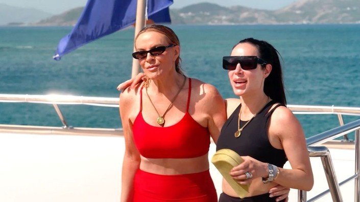 Two cast members in athletic wear and sunglasses on the yacht deck
