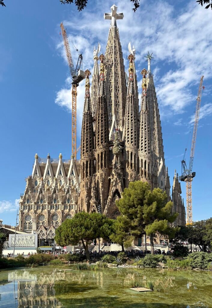 The Sagrada Familia's completed central tower topped with its white cross, tower cranes still in frame